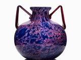 a purple vase with a red handle sitting on a white surface