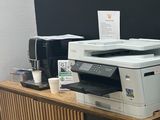 une photo d'une pièce dans laquelle se trouvent un réfrigérateur, une imprimante et d'autres fournitures de bureau