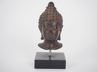 une tête de Bouddha en bronze posée sur un socle noir