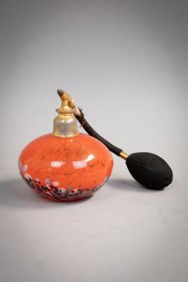 un petit flacon de parfum orange muni d'une poignée noire, posé sur une surface blanche