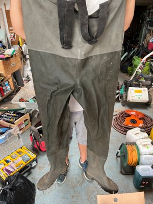 a man standing in a garage holding a pair of waders