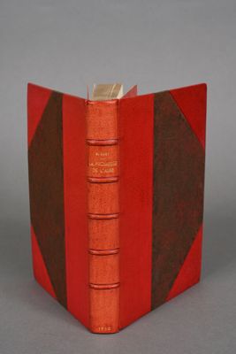 an old book with a red cover sitting on top of a table