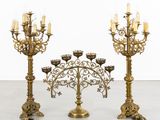 three brass candelabs with candles on each of them