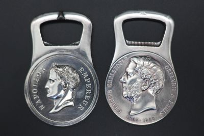 two silver coin shaped bottle openers on a black surface