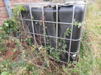 une valise noire posée dans l'herbe, près d'un mur de briques