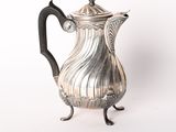 une cafetière ancienne en argent posée sur un support, sur fond blanc