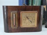 a wooden clock with a thermometer in front of a stack of books