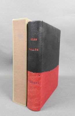 an old book sitting on top of a white table next to a red and black book