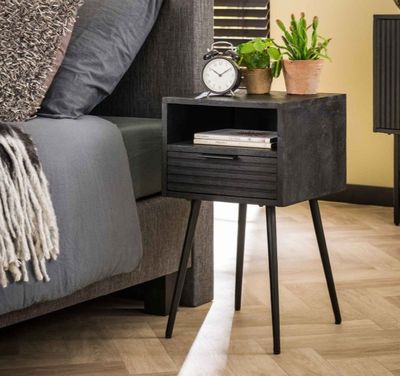 une petite table sur laquelle se trouve une horloge, à côté d'un lit