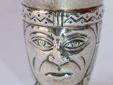 une coupe en argent ornée d'un visage, posée sur une table