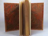 an open book with a red and brown cover sitting on top of a white table