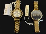 two gold watches sitting next to each other on a black surface