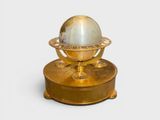un globe doré et blanc posé sur un socle, sur fond blanc