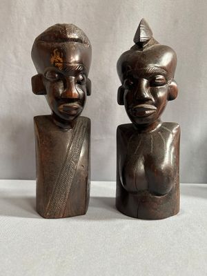 deux statues en bois représentant un homme et une femme, posées sur une surface blanche