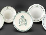 six white and blue plates with a crest on them on a black surface