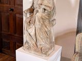une statue représentant une femme assise sur un socle à côté d'une chaise