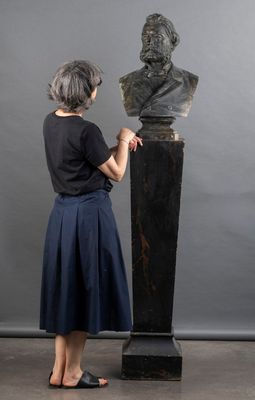 une femme debout à côté d'une statue représentant le buste d'un homme