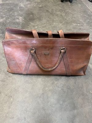 brown leather handbag on the floor next to a black cat