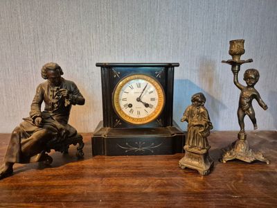 trois figurines en bronze posées sur une table à côté d'une horloge