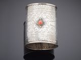 a close up of a silver cuff with a red stone in the center