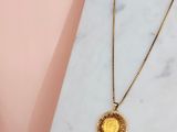 a gold coin necklace on a marble surface with a pink background