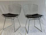 pair of chrome steel wire chairs with black leather seat cushions