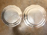 two silver plates sitting on a table next to each other