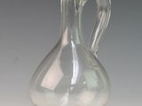 a clear glass vase with a curved handle on a table