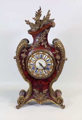une horloge rouge et dorée posée sur une surface blanche