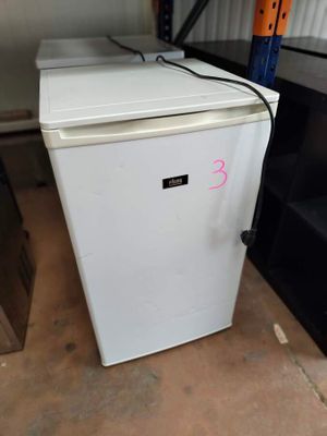a small white refrigerator sitting in a room next to a shelf