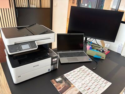 une imprimante et un ordinateur portable posés sur un bureau, à côté d'un écran