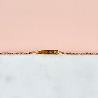 un bracelet en or avec une barre suspendue à une chaîne, sur fond rose