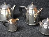 three silver teapots and two silver cups on a black surface
