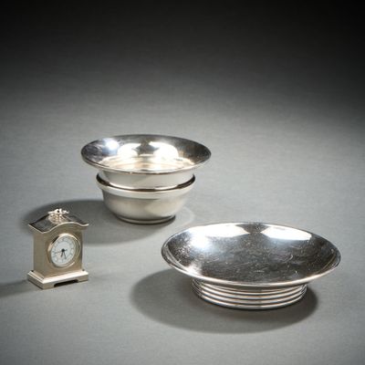 two silver dishes and a clock sitting on a table