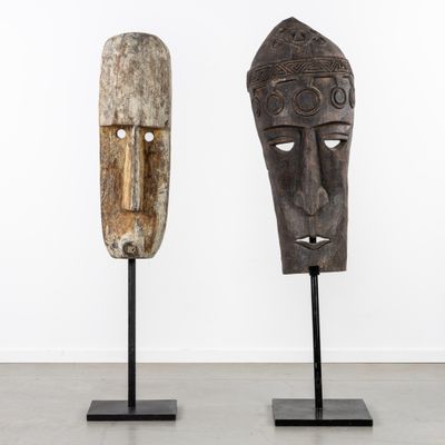deux masques en bois posés sur des socles dans une pièce aux murs blancs