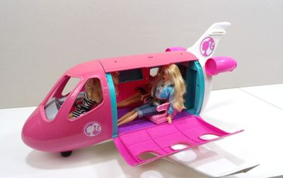 une poupée Barbie assise dans un petit avion rose avec deux petites filles à l'intérieur