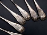 six silver spoons with designs on them on a black surface