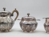 three silverplated teapots and a creamer on a white surface
