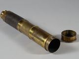 un télescope en laiton posé sur une surface blanche, à côté d'une tasse