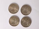 four coins are shown on a white surface, one of which has a picture of a woman and two men