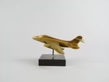 un avion doré posé sur un socle noir, sur fond blanc
