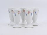 quatre tasses blanches ornées de motifs floraux sont alignées sur une surface blanche