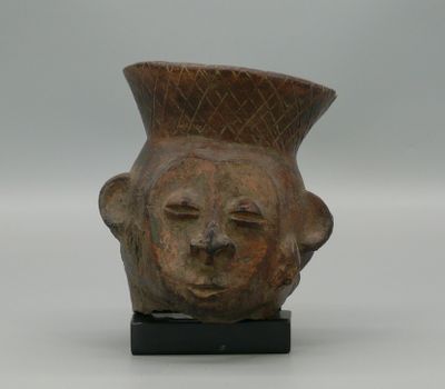un vase orné d'un visage, posé sur un socle
