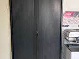une armoire noire dans un coin de la pièce, avec une imprimante posée dessus
