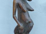 an image of a wooden statue of a woman sitting on a stool