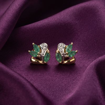 une paire de boucles d'oreilles en émeraude et diamant posées sur un tissu violet