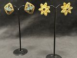 a pair of gold and turquoise flower earrings on a black stand