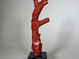une image représentant une sculpture rouge représentant une branche d'arbre posée sur un socle en marbre