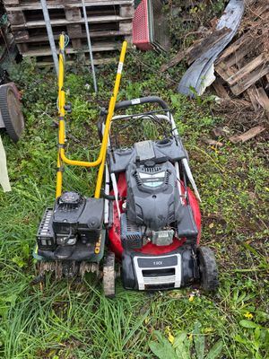 une tondeuse à gazon posée dans l'herbe, à côté d'un tas de bois