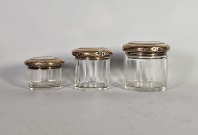 trois petits bocaux en verre avec des couvercles argentés, posés sur une surface blanche